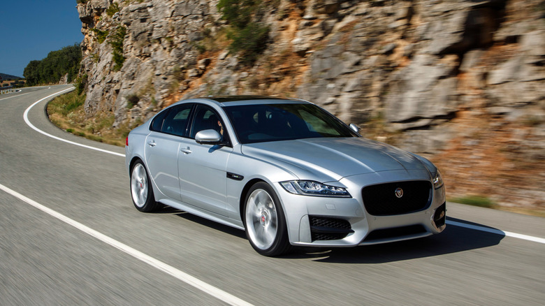 A front three quarters shot of a silver XF driving around a curve on a mountain road