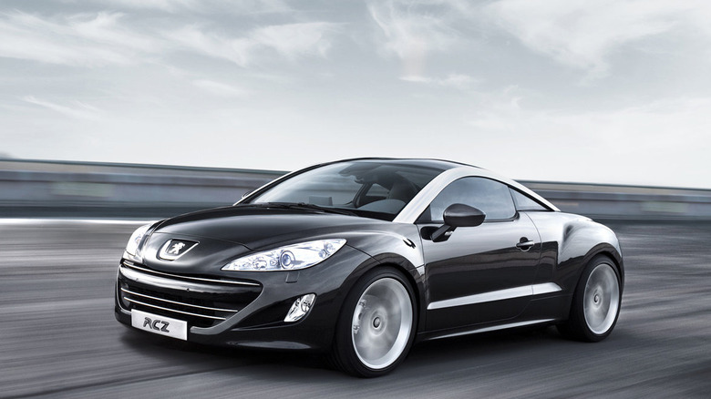 A black Peugeot RCZ driving very quickly on a road in front of a cloudy sky