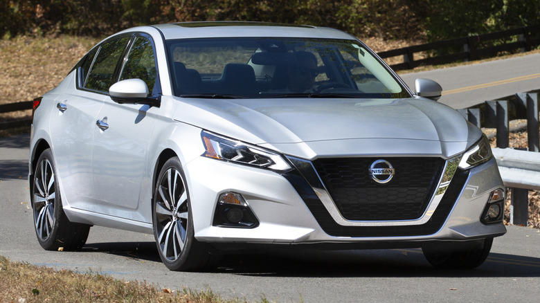 A gray 2020 Nissan Altima driving on a paved road in a wooded area