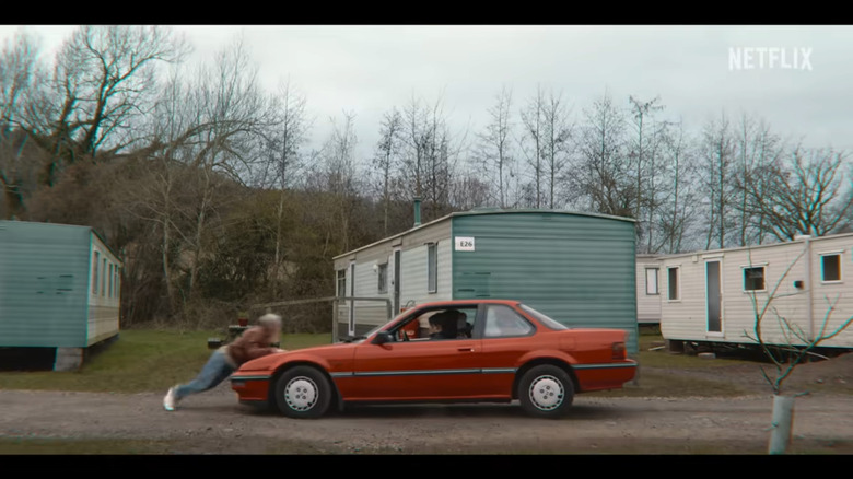 Screenshot from Sex Education where a red Chevy Beretta hits a woman on a road in a trailer park.
