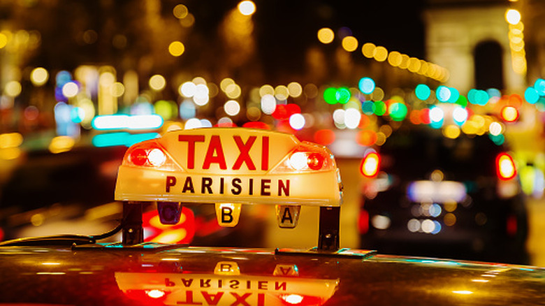 A taxi sign illuminateed on the streets of Paris, the arc de triomph in the background