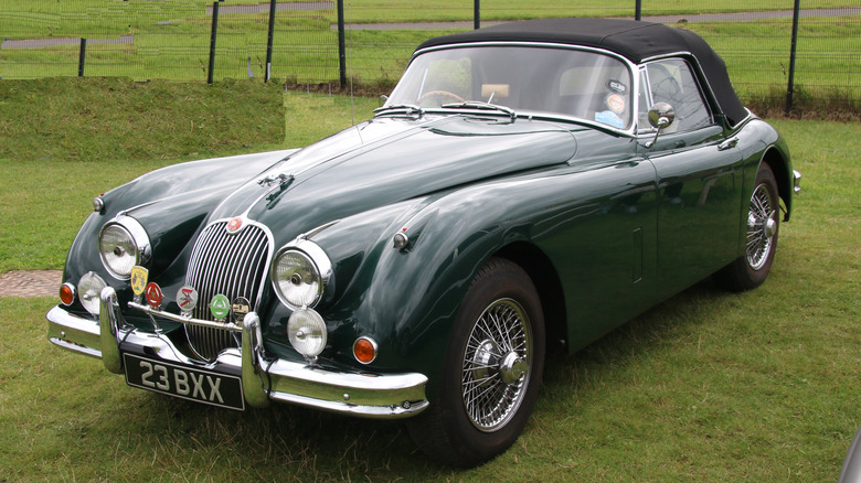 A British racing green Jaguar XK150 parked on a grass lawn.