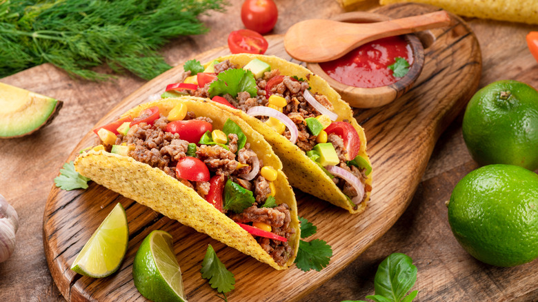 Mexican meat tacos or beef stuffed tortillas and lime slices near them on wooden serving board.