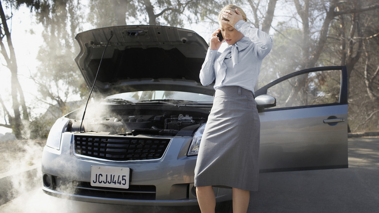A woman experiencing a breakdown with what looks like a Nissan Sentra in a forested environment.