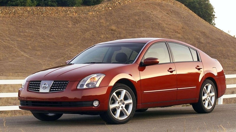 Front three quarters shot of a burgundy 2004 Nissan Maxima parked in front of a brown grassy hill