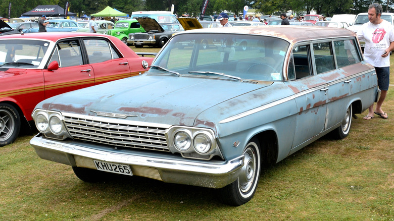 Front three quarters shot of a rusty blue '62 Chevy wagon parked on grass at a car show