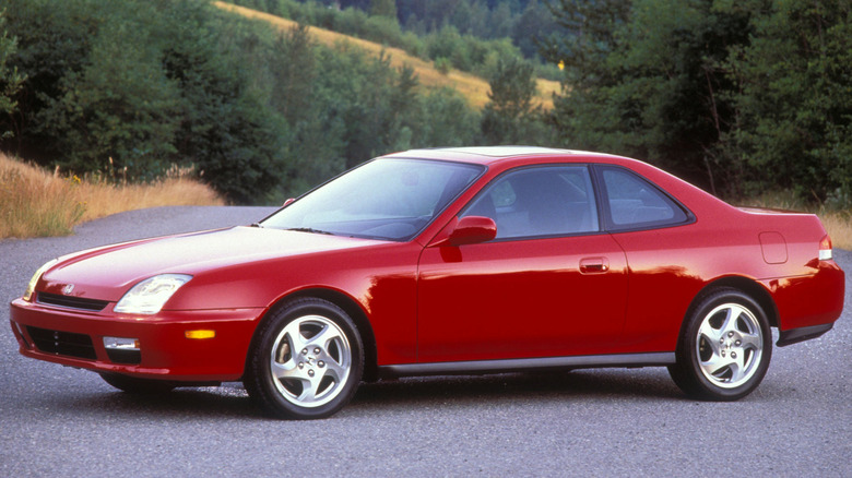 Front three quarters shot of a red Prelude parked on asphalt in front of green trees and brown grasses