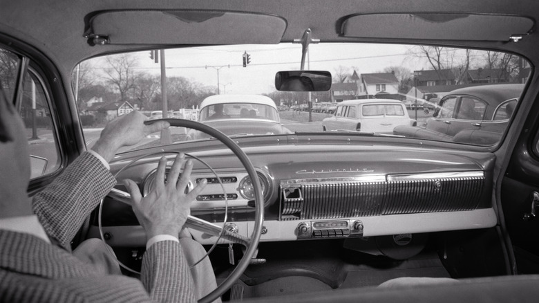 A black and white vehicle sitting in traffic, a man angrily hitting the horn