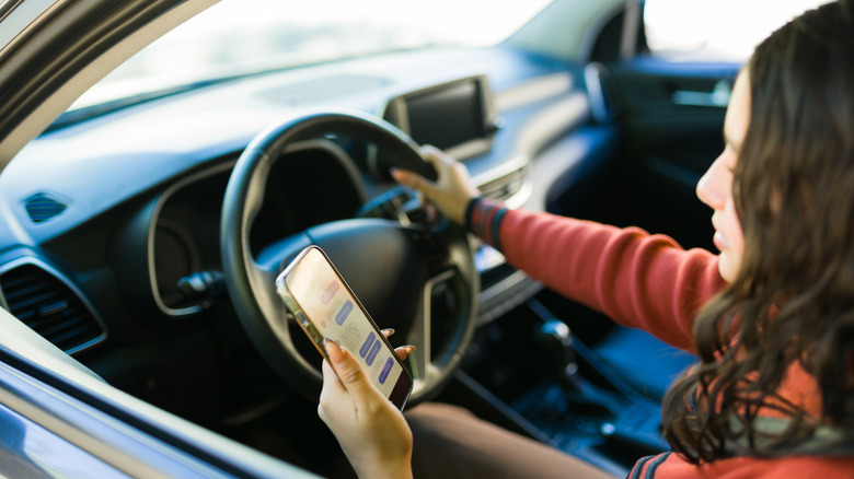 teen girl checking her phone behind the wheel of her car