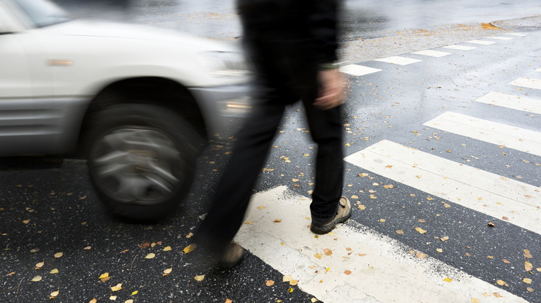 man crossing the road in a cross walk on a fall day as a car comes across him.