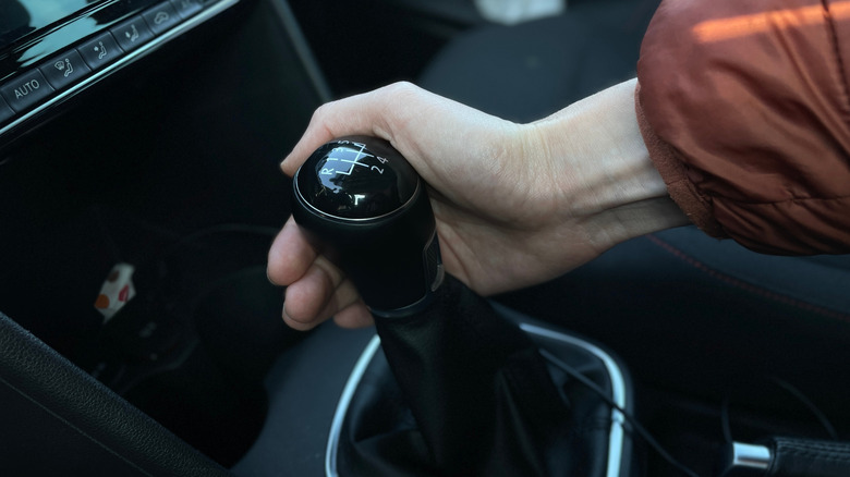 Driver's hand shifting a manual gear stick inside a car. Close-up view of a person changing gears while driving. Concept of manual transmission, driving control, automotive interior, and car operation  by: Alexandra Alex