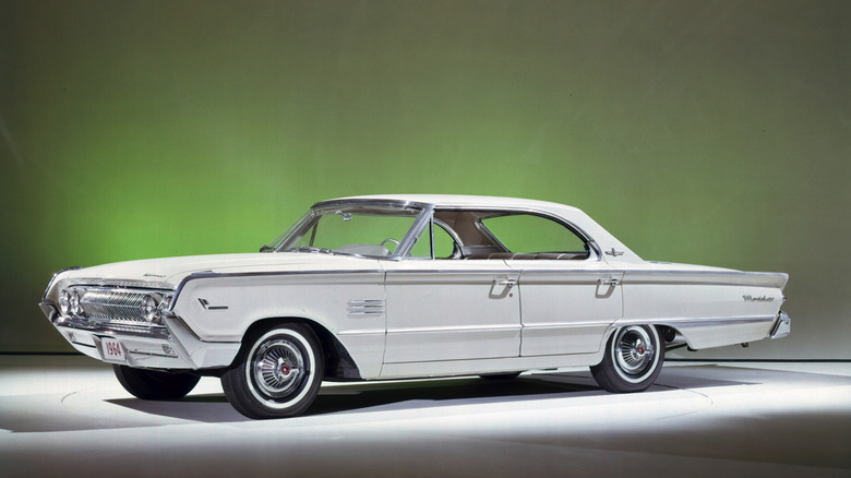 A pristine, white 1964 Mercury Marauder on a white platform in a studio with green lighting behind it.