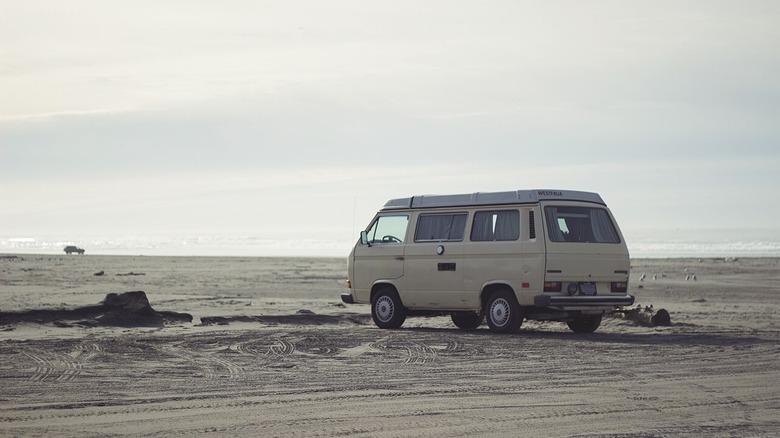 A pale yellow Volkswagen Vanagon on a beach on a slightly overcast day with some sun for a washed out look.