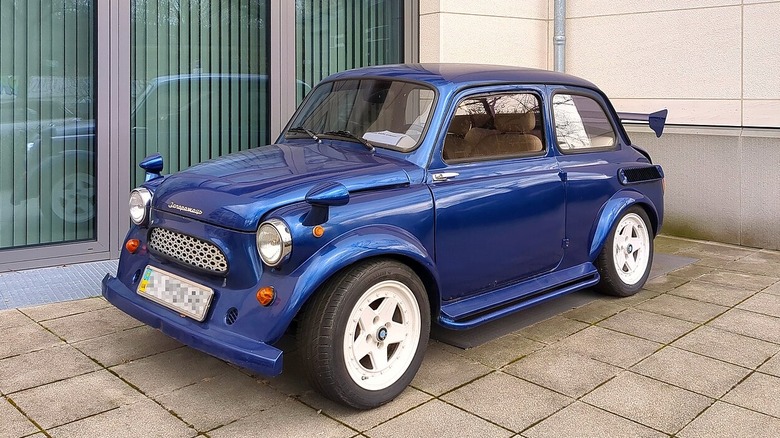 A blue coupe Auto ZAZ-965 known as the SAZ Zaporozhets in front of a modern building in Germany.