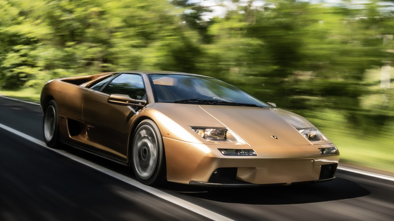 A gold Lamborghini diablo speeding down a sunny road