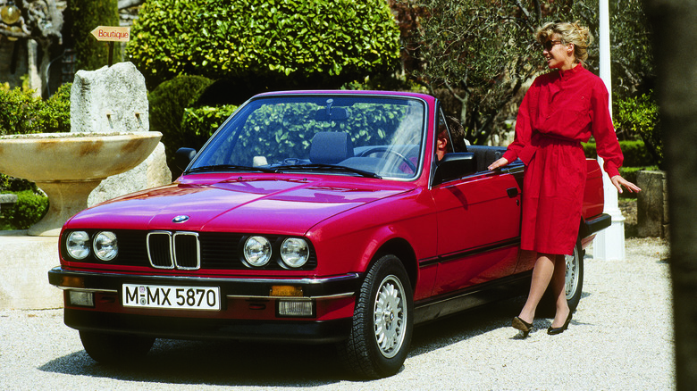 Front 3/4 view of a red BMW 3 Series convertible with a woman posing next to it