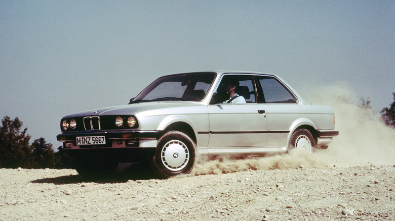 Front 3/4 view of a silver BMW 325iX driving in dirt