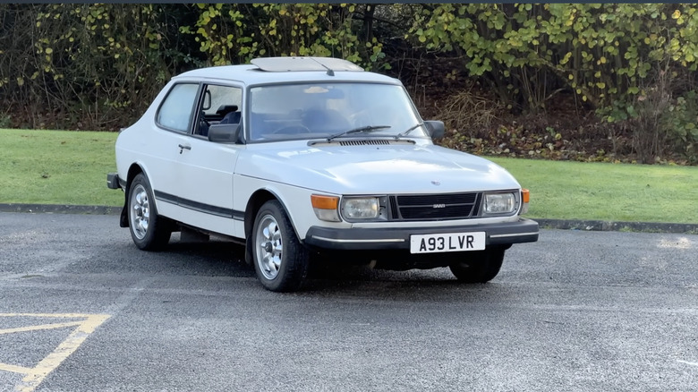 a saab 1978 99 EMS  parked in a parking lot in front of green bushes