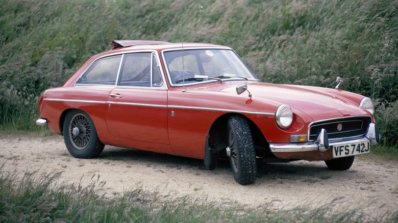 a red mgb gt parked in sand surrounded by grass