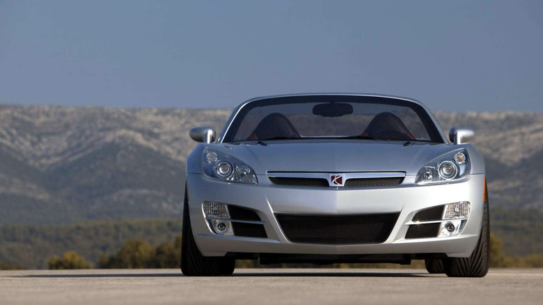 A saturn sky sports car parked in the desert with mountains rolling in the background and a cloudless blue sky