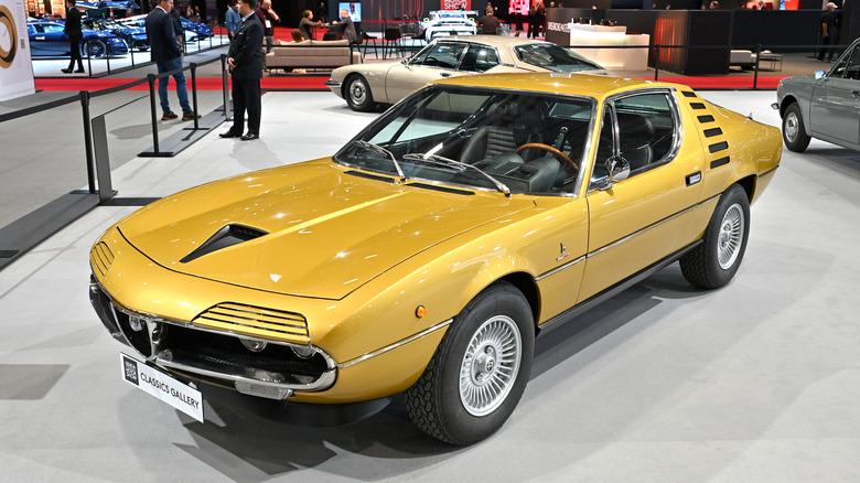 a gold Alfa Romeo Montreal sitting on an auto show floor