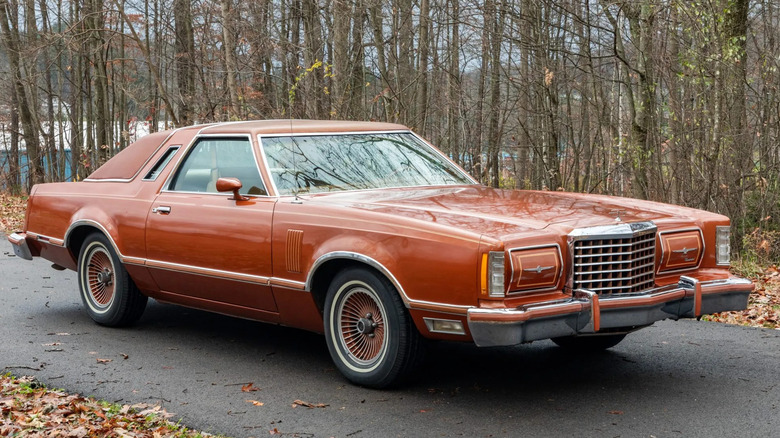 Front three quarters shot of a copper '78 Ford Thunderbird parked on asphalt in front of bare trees