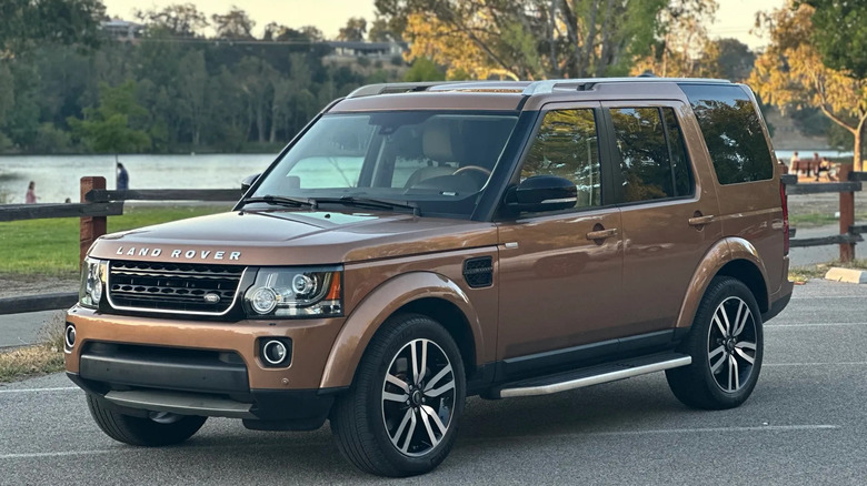 Front three quarters shot of a copper Land Rover LR4 parked in front of a lake and trees