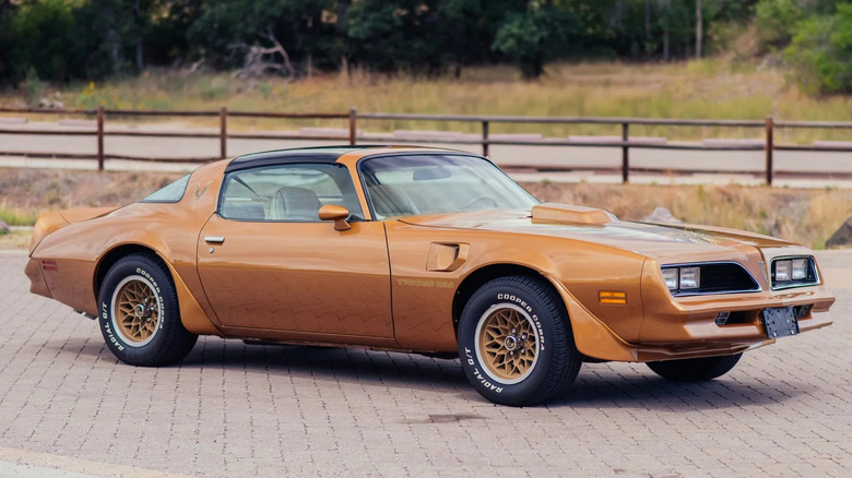 Front three quarters shot of a bronze '78 Pontiac Firebird Trans Am parked on brick in front of a fence