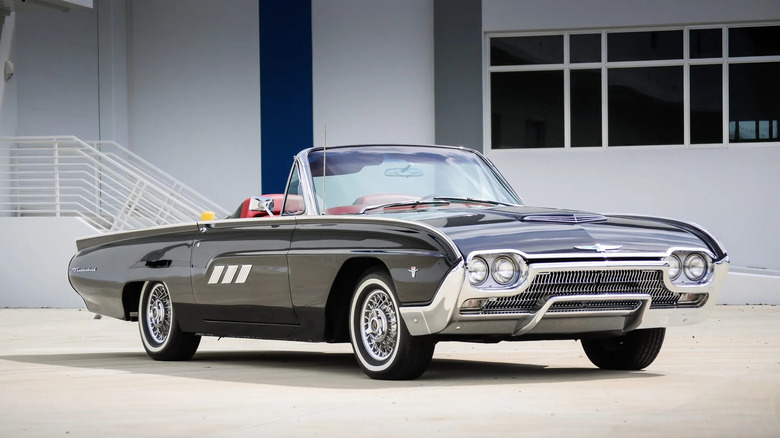 A black Ford Thunderbird Sports Roadster with its top down parked on concrete in front of a white building