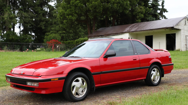 Front three quarters shot of a red 1990 Prelude Si parked on dirt surrounded by grass and trees