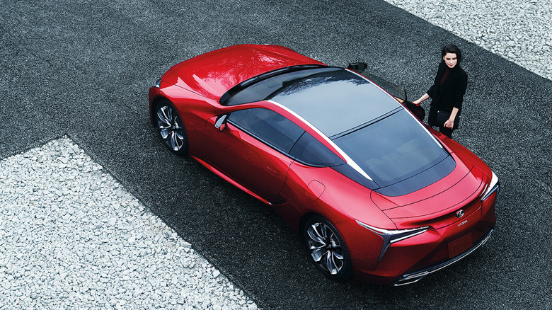 An overhead shot of a red LC500 parked on asphalt with a woman wearing black opening the door