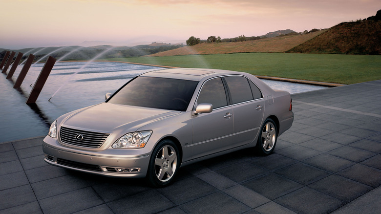 A front three quarters shot of a silver LS430 parked in front of a fountain and grassy hills at dusk