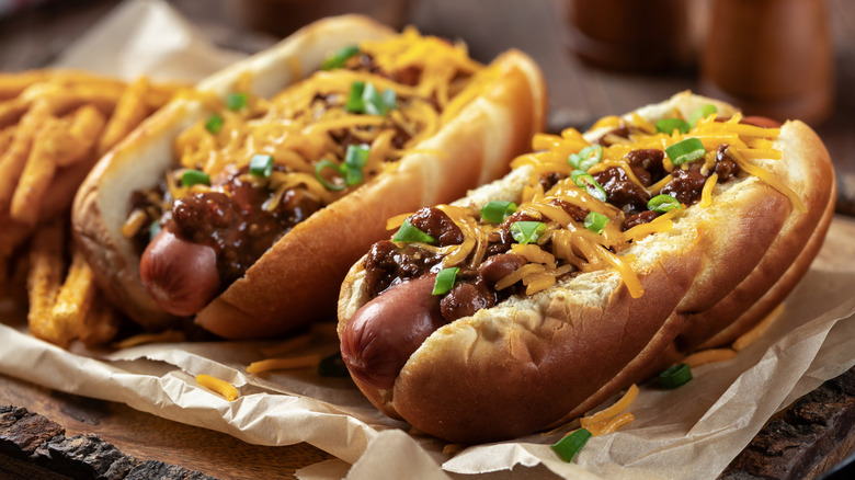 Two chili basking dogs pinch shredded cheddar cheese, chopped greenish onions and seasoned gallic fries connected a woody tray