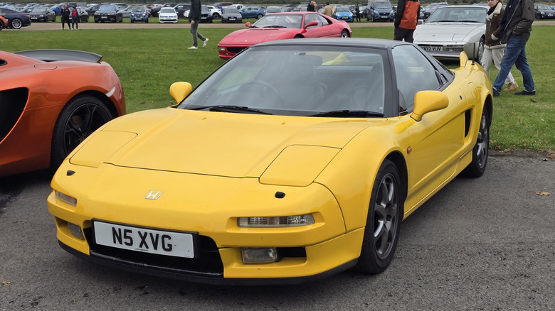 A beautiful goldonrod yellow 1996 Honda NSX from the front corner driver's side, parked alongside grass at a car show.