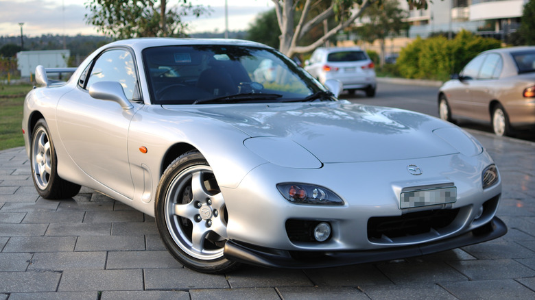A bright silver Mazda RX-7 parked on large bricks.