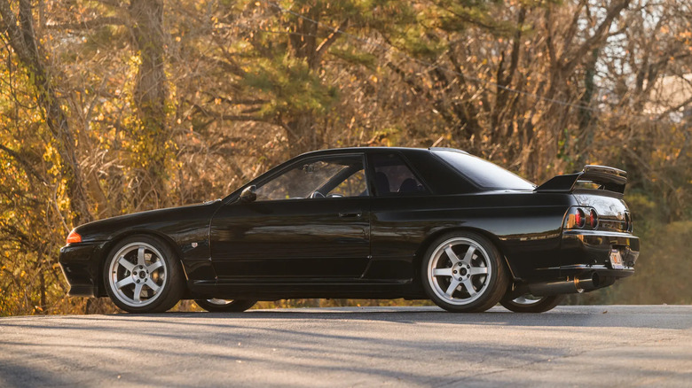A black, 1991 Nissan Skyline GT-R (R32) on a paved road in a forested area.