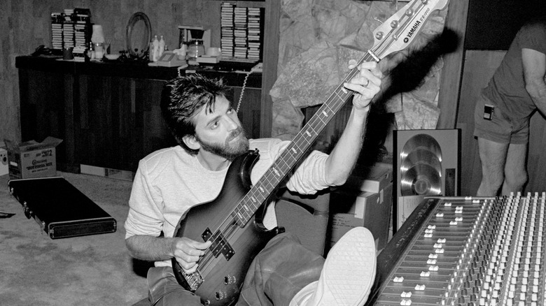 a black and white image of a man holding a yamaha guitar sitting at a mixing board.