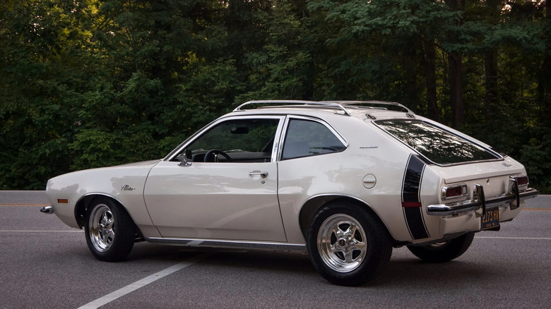 Rear three-quarters shot of a white Ford Pinto coupe with a black stripe parked in front of plants