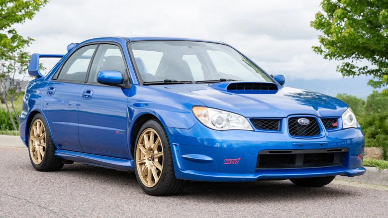 Front three-quarters shot of a blue Hawkeye Subaru WRX STI parked in front of trees