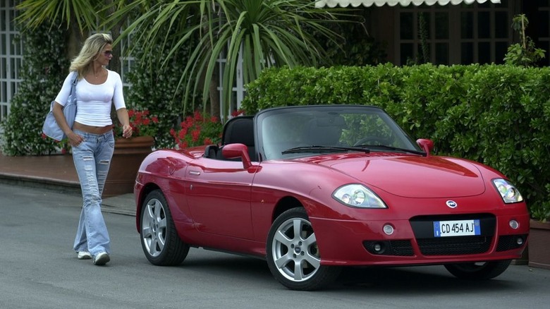 A woman standing next to a red Fiat Barchetta