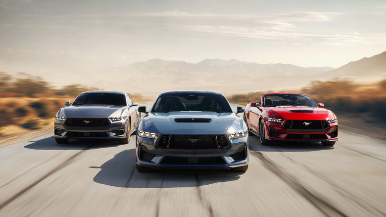 A head-on shot of three Ford Mustangs driving on a desert road