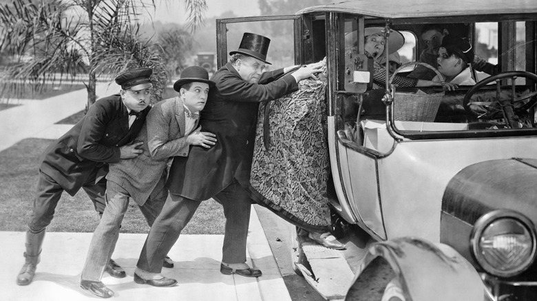 (Original Caption) Three men pushing a stout woman into a car filled with children. Undated movie still. BPA2# 2989