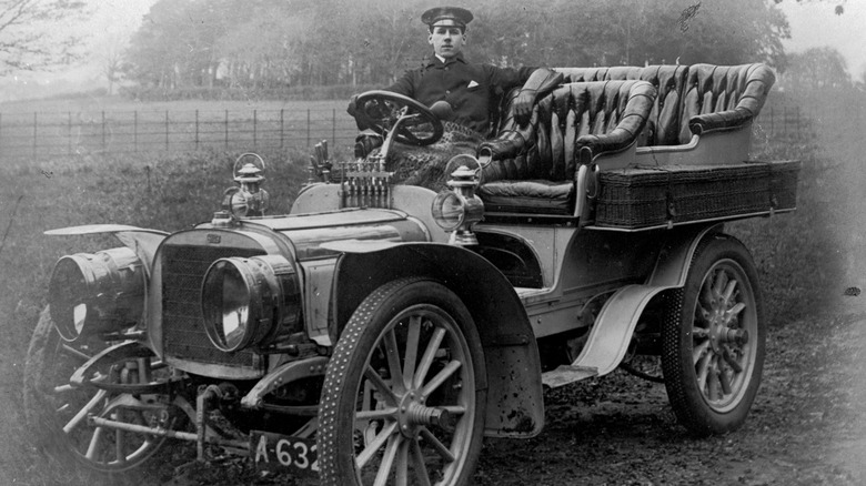 circa 1910: A chauffeur sits at the wheel of an early motor car. (Photo by Sean Sexton/Getty Images)