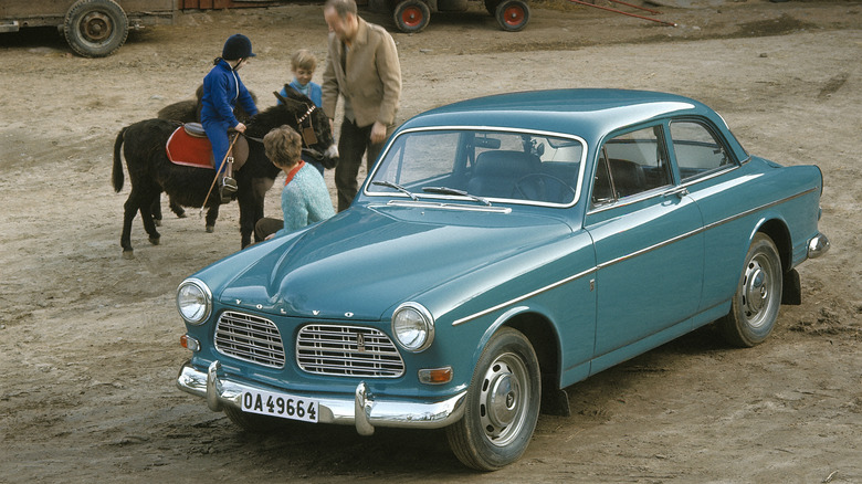 A blue Volvo Amazon with people and a burro next to it