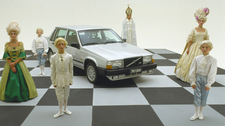A silver Volvo 740 Turbo sedan surrounded by people dressed like Marie Antoinette