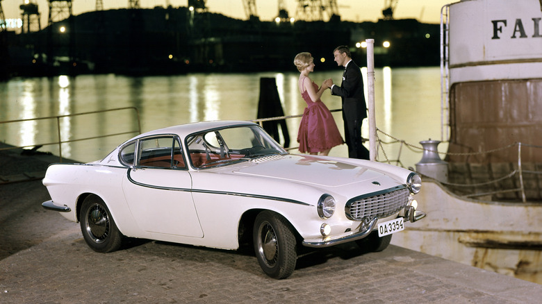 A white Volvo P1800 parked on a pier