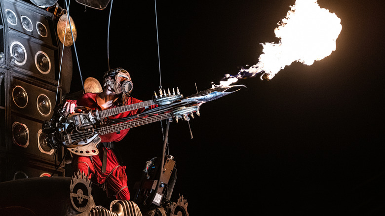 Melbourne, Victoria Australia - 08242019: Mad Max Festival Mad Max Doof Warrior musician playing the guitar with fire coming out of it at night surrounded by speakers.