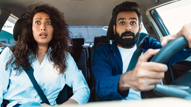 Scared young couple looking at road with shocked expression, having risk of traffic accident, driving car and braking hard, looking at crash or animal on the road
