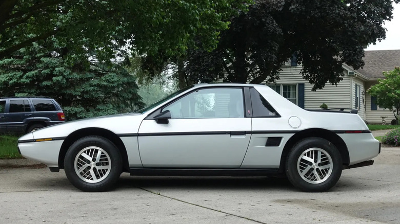 Side view of a silver '85 Fiero parked in front of trees and a white house