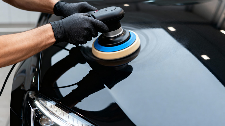 A professional detailer uses a polishing machine to restore the shine of a black car's paintwork